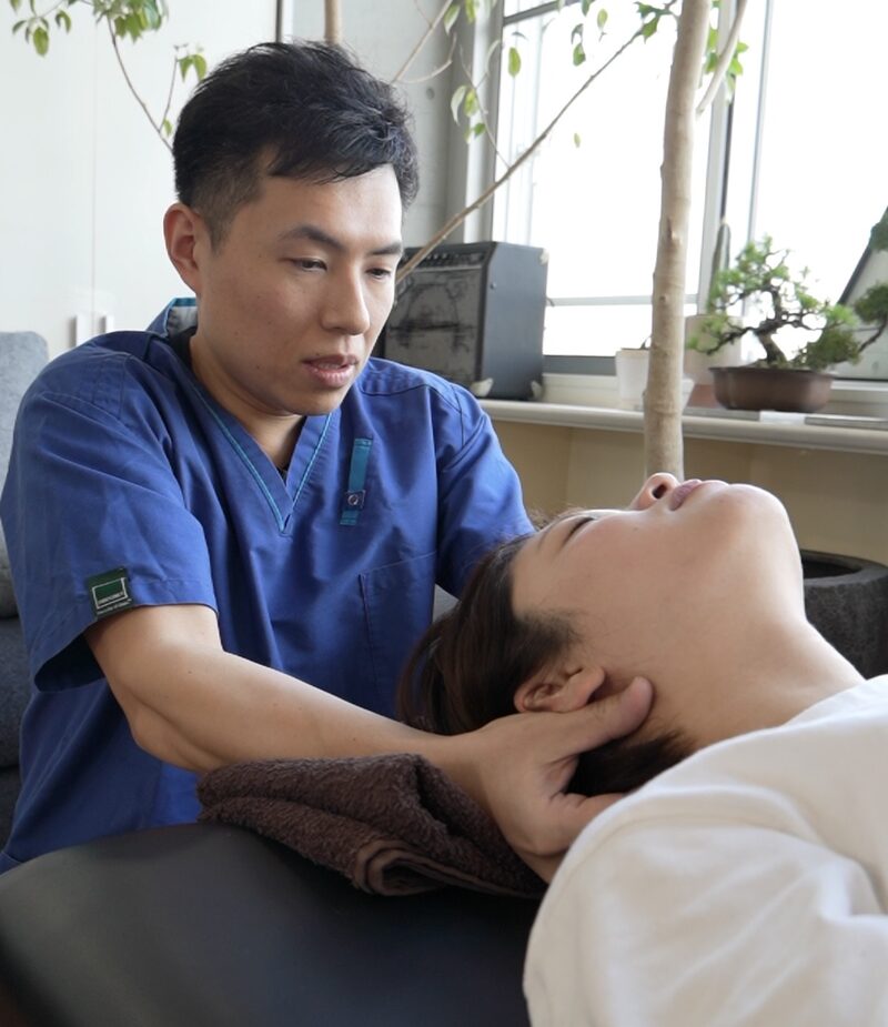 仰向けの女性の首を、施術者が手で支えている様子